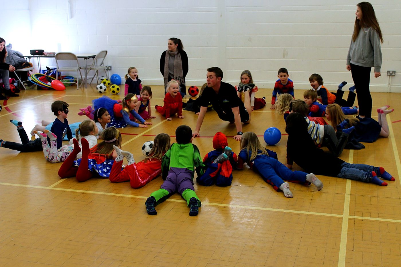 Children in superhero outfits taking part in active circle games at a TNT party