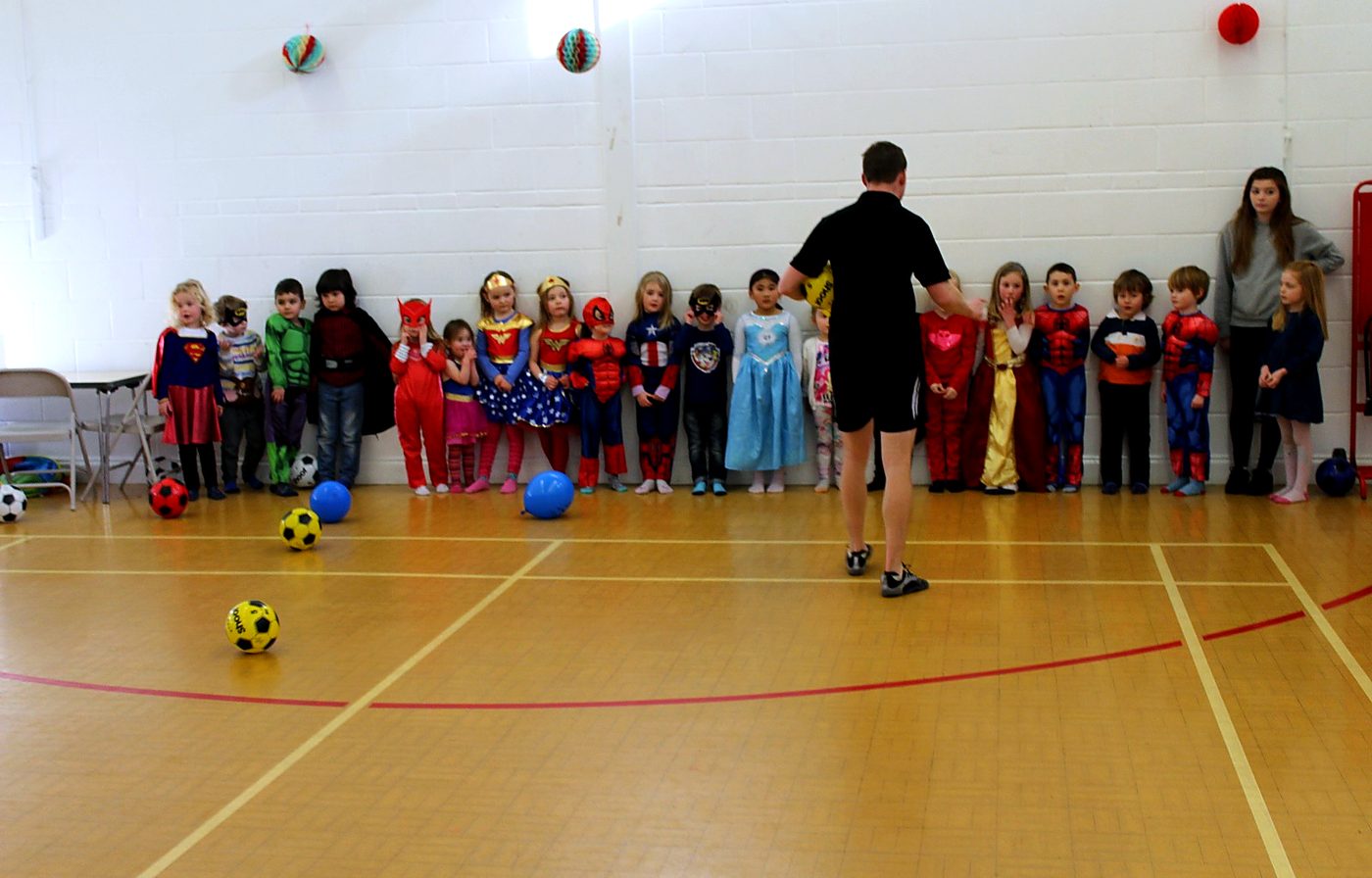 Children in superhero costumes lined up for games at a TNT party session
